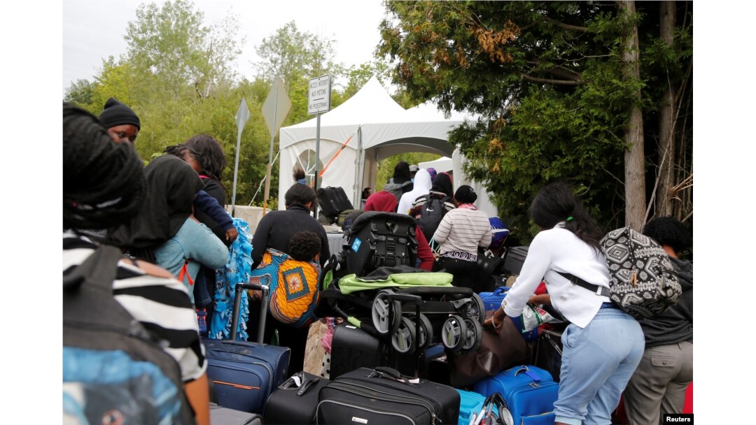 FILE - A line of asylum-seekers who identified themselves as from Haiti, wait to enter into Canada from Roxham Road in Champlain, New York, Aug. 7, 2017.