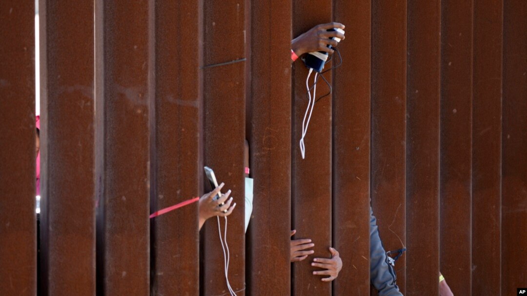 FILE - Migrants waiting to apply for asylum between two border walls hold out phones in hopes of getting a charge on May 11, 2023, in San Diego. 