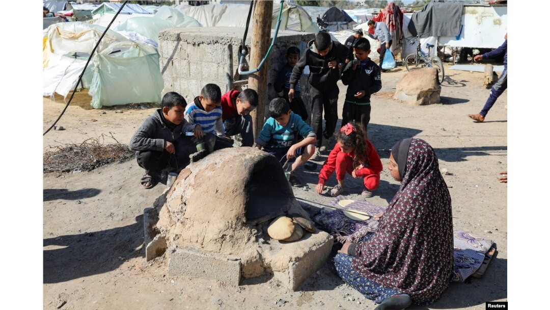 A Palestinian woman bakes bread as children sit next to her, while Gaza residents face crisis levels of hunger and soaring malnutrition, in Khan Younis in the southern Gaza Strip, Jan. 24, 2024.