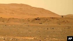 FILE - This April 30, 2021, image taken by the Mars Perseverance rover shows the Ingenuity helicopter, right, flying over the surface. Data gathered from the planet indicate there could be quite a bit of water well below the surface. (NASA via AP)