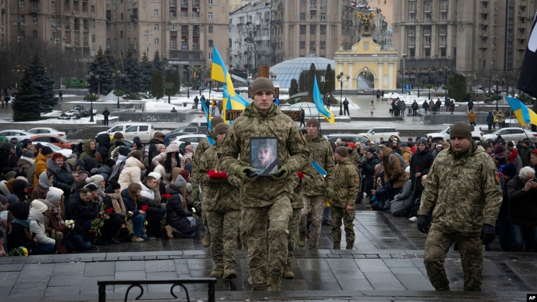 People kneel as soldiers carry the coffin of Ukrainian serviceman and poet Maksym Kryvtsov — who was killed in a battle with Russian troops — during the funeral ceremony for Kryvtsov in St. Michael Cathedral in Kyiv, Ukraine, Jan. 11, 2024.