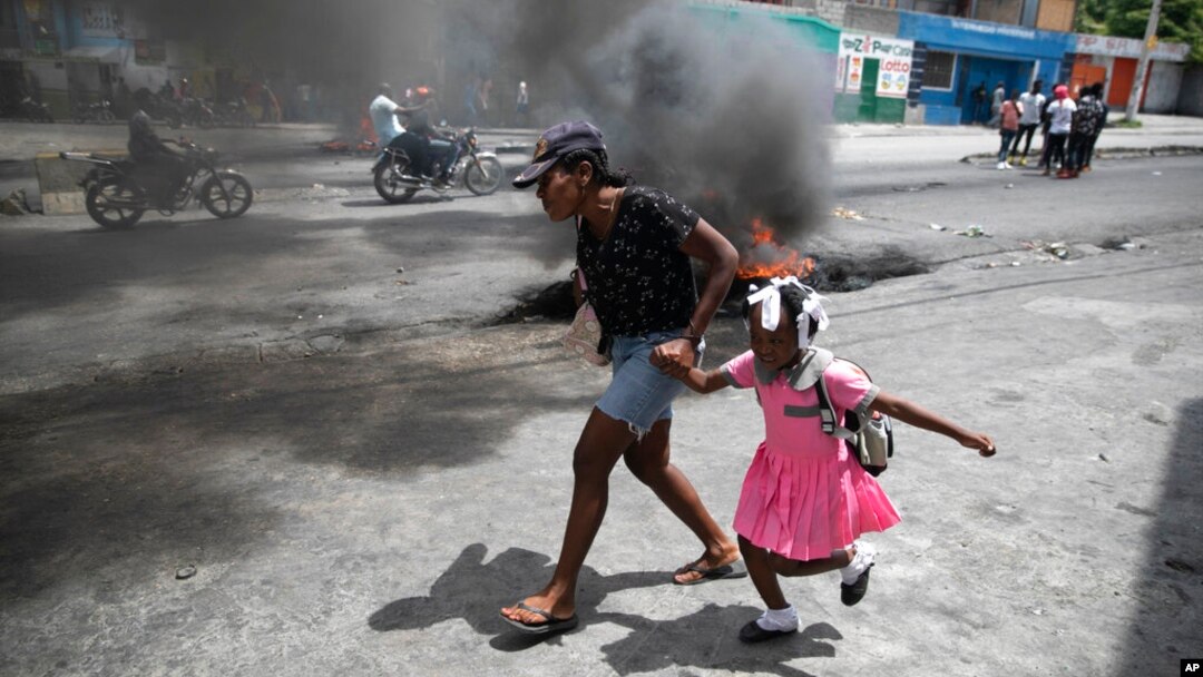 FILE - A woman guides a child past a demonstration against increasing violence in Port-au-Prince, Haiti, March 29, 2022.