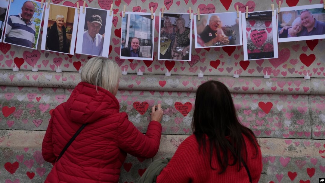 FILE: Family members write a message to two sisters who died of COVID on the National Covid Memorial wall in London, March 29, 2022.