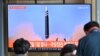 People watch a television screen showing a news broadcast with file footage of a North Korean missile test, at a railway station in Seoul on May 4, 2022. - North Korea fired a ballistic missile on May 4, South Korea's military said, just a week after lead
