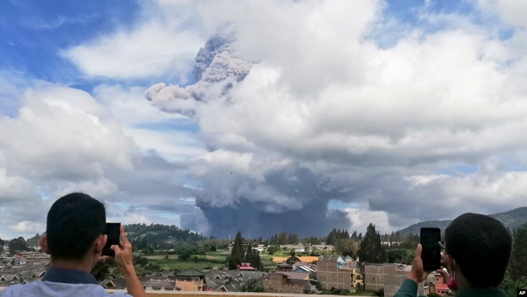 Men use their mobile phones to take photos as Mount Sinabung spews volcanic materials into the air as it erupts, in Karo, North Sumatra, Indonesia, Aug. 10, 2020.