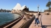 FILE - A lone tourist poses for a photo in Circular Quay in Sydney on March 20, 2020, after Australia moved to seal off its borders the day before, announcing unprecedented bans on entry for non-residents.