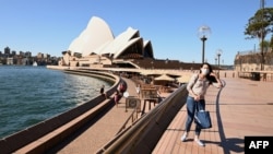 FILE - A lone tourist poses for a photo in Circular Quay in Sydney on March 20, 2020, after Australia moved to seal off its borders to help stop the spread of COVID-19.
