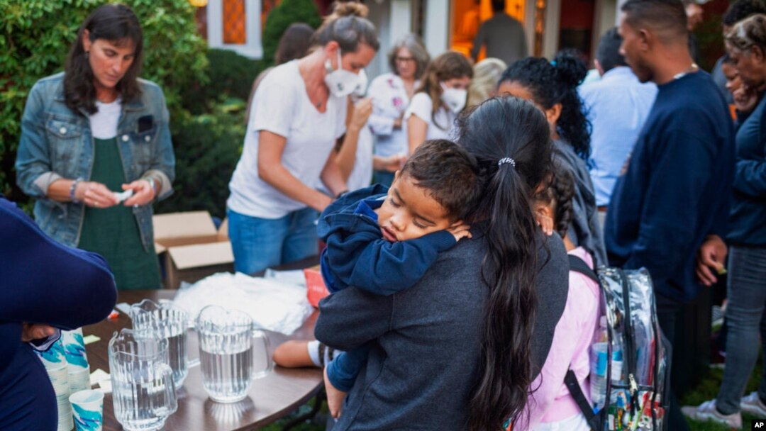A woman, part of a group of immigrants who had just arrived, holds a child as they are fed outside St. Andrews Episcopal Church, Sept. 14, 2022, in Edgartown, Massachusetts, on Martha's Vineyard.