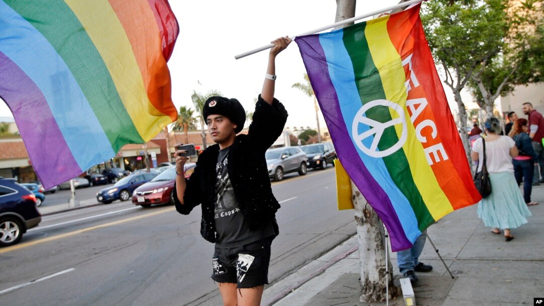 FILE - Bryan Kimpton, a supporter of the School Success and Opportunity Act (AB1266) waves a flag while celebrating at a rally organized by San Diego LGBTQ rights organizations Canvass for a Cause, SAME Alliance, and Black and Pink.