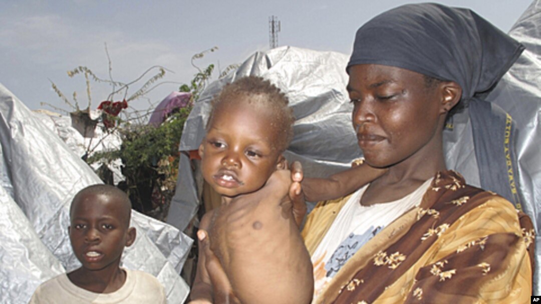 An Somali woman and her children displaced by famine, wait to receive food aid near their makeshift shelters in Mogadishu, Somalia, Friday, July 22, 2011