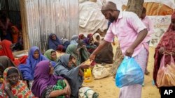 Wasomalia waliotoroka maeneo yanayokumbwa na ukame wakipewa msaada wa chakula , kwenye kambi ya wakimbizi wa ndani, kwenye vitongoji vya Mogadishu, Juni 30, 2022.