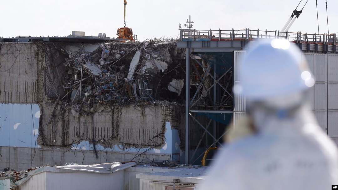 A member of the media tour group wearing a protective suit and a mask looks at the No. 3 reactor building at Tokyo Electric Power Co's (TEPCO) tsunami-crippled Fukushima Daiichi nuclear power plant in Okuma, Fukushima Prefecture, Japan, Feb. 10, 2016. 
