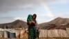 FILE - An internally displaced Afghan girl carries a child near their shelter at a refugee camp on the outskirts of Kabul, Afghanistan June 20, 2019. 