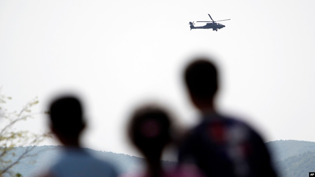 Migrants watch a helicopter of Greek army during exercises near the makeshift camp at the northern Greek border point of Idomeni, Greece, April 14, 2016.