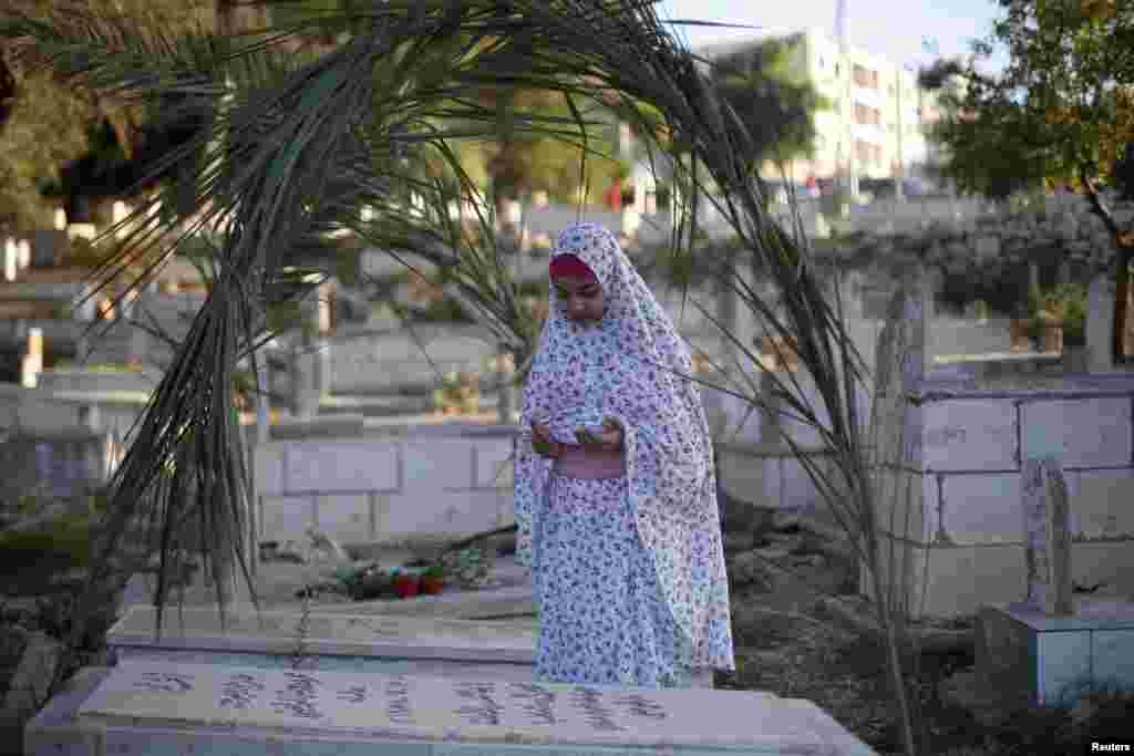 A Palestinian girl prays next to a grave at a cemetery in the West Bank city of Ramallah on the first day of Eid al-Fitr, August 8, 2013.