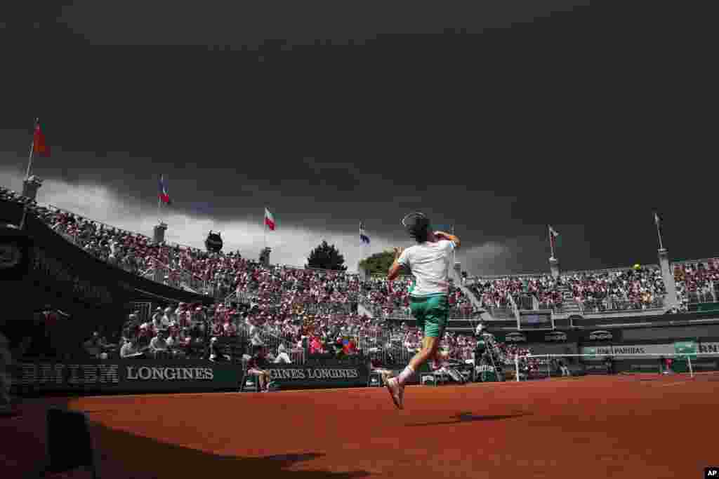 Dark clouds approach court one as Austria's Dominic Thiem plays a shot against Steve Johnson of the U.S. during their third round match of the French Open tennis tournament at the Roland Garros stadium, in Paris, France.