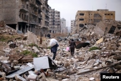 People walk amid the rubble as they carry belongings that they collected from their houses in the government controlled area of Aleppo, Syria, Dec. 17, 2016.
