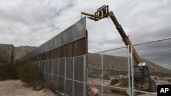 FILE - Workers raise a taller fence along the Mexico-US border between the towns of Anapra, Mexico and Sunland Park, New Mexico, Nov. 10, 2016. For almost two decades, a Mass has been celebrated there on the Day of the Dead to remember migrants who have died trying to cross the fence.