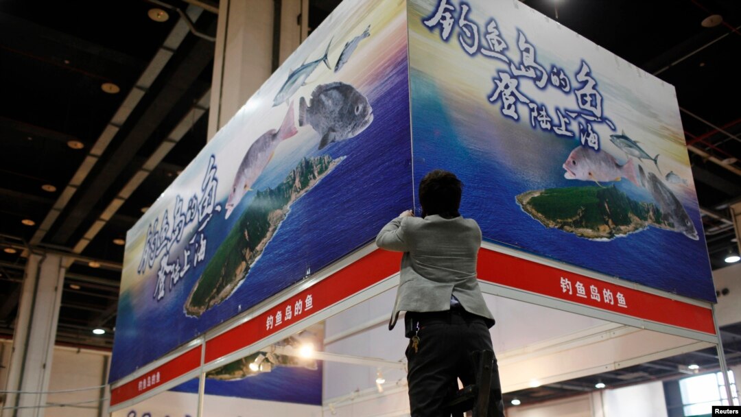FILE - A vendor installs a poster above his booth, which sells fishes caught by Zhejiang fishermen in waters near disputed islands, known as Diaoyu in China and Senkaku in Japan, during a food exhibition in Shanghai.