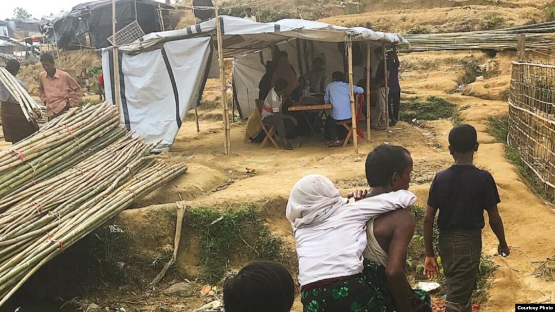 Rohingya refugees walk along a litter-strewn path next to makeshift tents at a camp in Bangladesh.