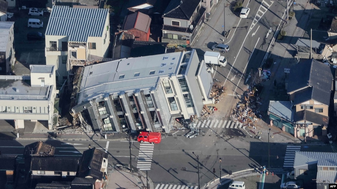 This aerial photo provided by Jiji Press shows a rescue vehicle parked next to a seven-story building that fell over in Wajima, Ishikawa prefecture on Jan. 2, 2024, a day after a major 7.5 magnitude earthquake struck Japan's Noto region.