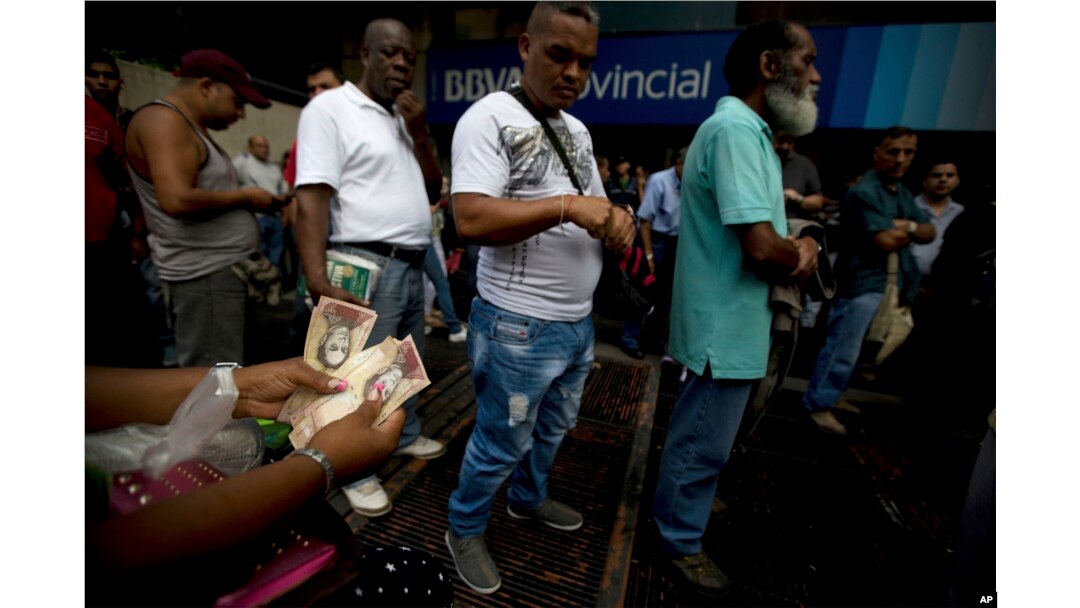 A woman counts her 100-bolivar notes while standing in line outside a bank in Caracas, Venezuela, Tuesday, Dec. 13, 2016.