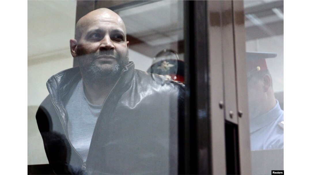 FILE - Sergei Khadzhikurbanov is escorted into a glass-walled cage before a court hearing in Moscow, June 3, 2013. Convicted in the assassination of journalist Anna Politkovskaya, he has been pardoned after fighting in the war in Ukraine.