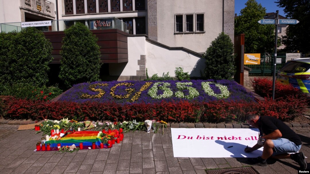 A man writes on a placard near tributes placed on the ground following an incident in which three people were killed by a man who randomly stabbed passers-by with a knife at a city festival in Solingen, Germany, on Aug. 24, 2024.