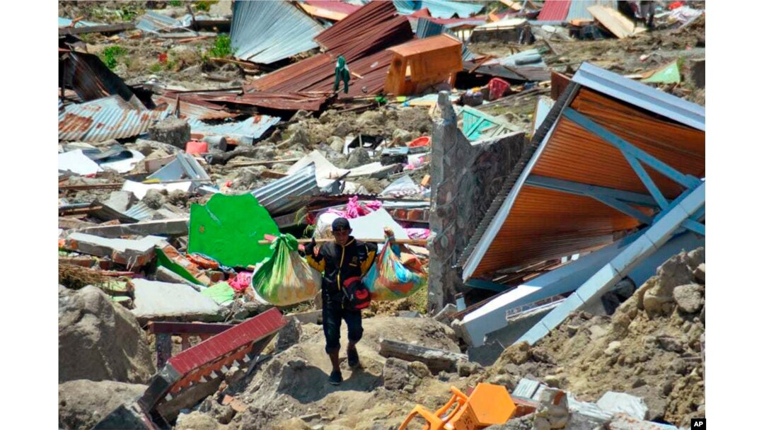 A man carry items he saved from the rubble following a major earthquake and tsunami in Palu, Central Sulawesi, Indonesia, Monday, Oct. 1, 2018.
