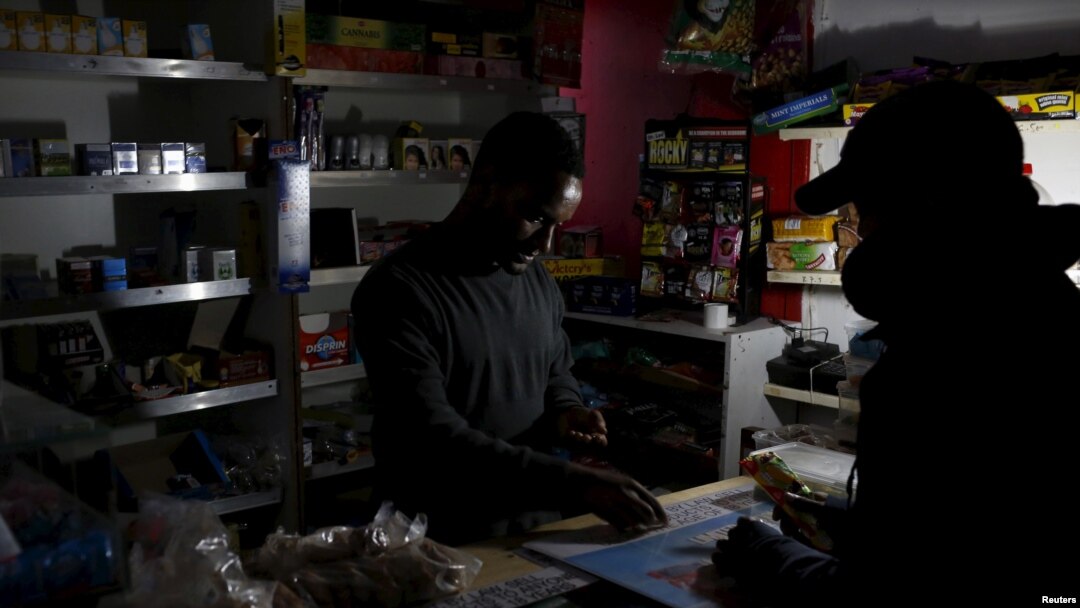 A shopkeeper counts change by the light of a battery-powered lamp during a load-shedding electricity blackout in Cape Town, South Africa, April 15, 2015.