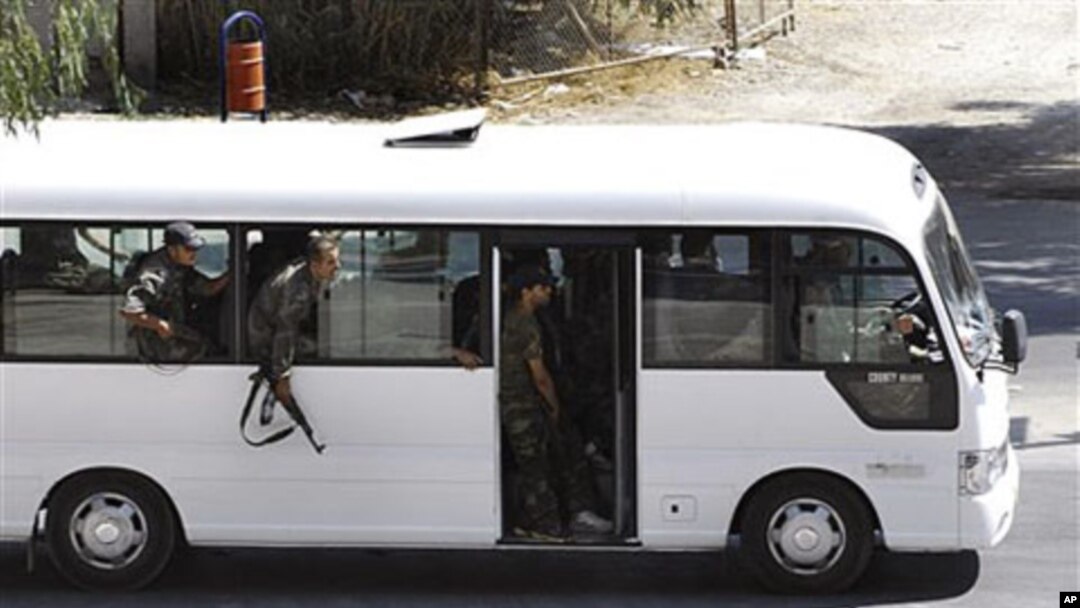In this citizen journalism image, Syrian security forces lean out of a bus windows as they withdraw from the Damascus suburb of Saqba, Syria, following a campaign of raids and arrests that are part of a nationwide crackdown against protesters calling for