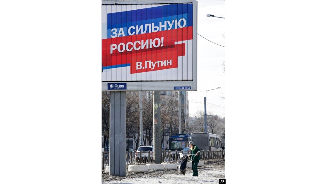 A municipal worker collects rubbish under an election poster for Russian President Vladimir Putin in St. Petersburg, Russia, March 17, 2018. The sign on poster reads: "For the strong Russia! Vladimir Putin."