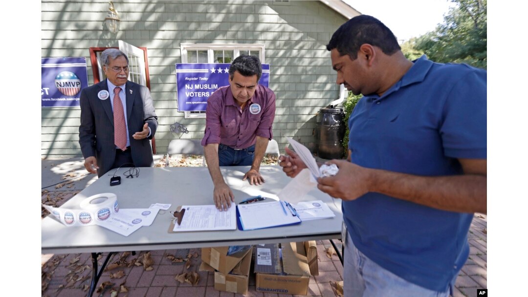 In this Sept. 23, 2016, photo, Mohammad Ali Chaudry, left, president of the Islamic Society of Basking Ridge, New Jersey, and Shawn Butt provide voter registration information to Shahul Feroze, right, after a prayer service.
