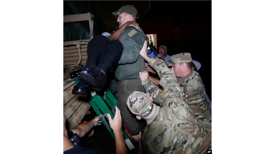 National Guard members help brace a rescuer as he lowers a resident from a rescue vehicle, Aug. 28, 2017 in Lake Charles, La., after flooding from Tropical Storm Harvey's almost constant rain over the last two days overcame the city's drainage system.
