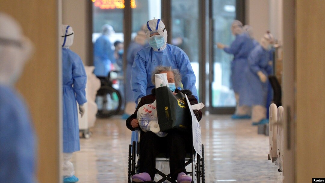 FILE - A medical worker in a protective suit moves a coronavirus patient in a wheelchair at a hospital in Wuhan, Hubei province, China, Feb. 10, 2020.