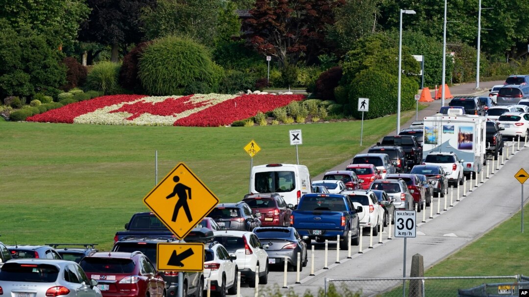 A line of vehicles wait to enter Canada at the Peace Arch border crossing in view of a Canadian flag made of flowers Monday, Aug. 9, 2021, in Blaine, Wash. 