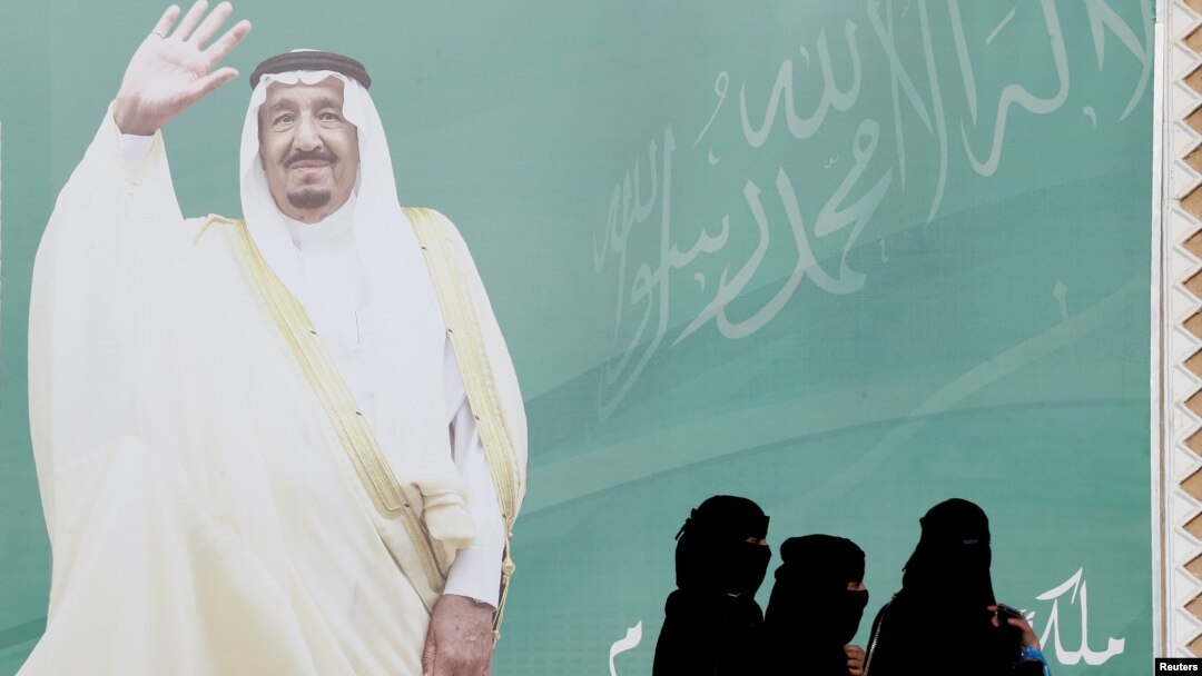 FILE - Women walk past a poster of Saudi Arabia's King Salman bin Abdulaziz Al Saud during Janadriyah Cultural Festival on the outskirts of Riyadh, Saudi Arabia Feb. 12, 2018.