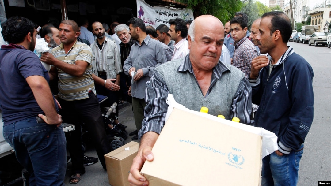 FILE - Displaced Syrians collect rations provided by the World Food Program in front of a distribution center in Damascus, Oct. 19, 2014.