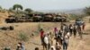 FILE - Villagers return from a market to Yechila town in south central Tigray walking past scores of burned vehicles, in Tigray, Ethiopia, July 10, 2021.