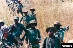 FILE - UNITA troops walk through a field, 20 miles from the front line, at Munhango, Angola, April 29, 1986. The UNITA forces, led by Jonas Savimbi, were engaged in a guerilla war against the Angola government.