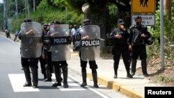 FILE - Nicaraguan police officers block journalists working outside the house of opposition leader Cristiana Chamorro after prosecutors sought her arrest for money laundering and other crimes, in Managua, Nicaragua, June 2, 2021.
