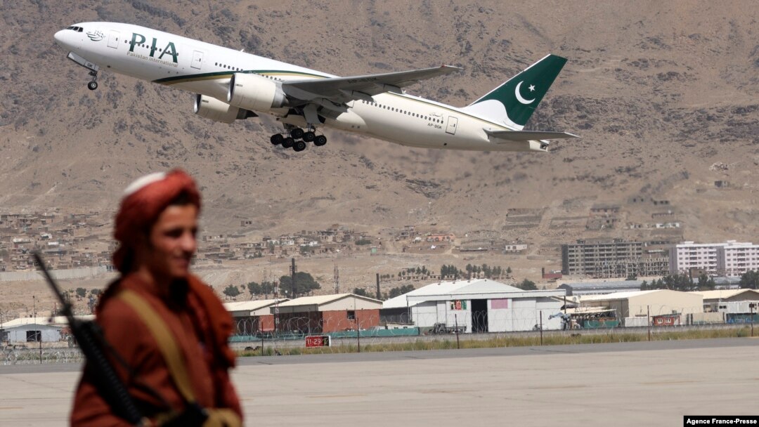 FILE - A Taliban fighter stands guard as a Pakistan International Airlines plane, the first commercial international flight to land since the Taliban retook power, takes off at the airport in Kabul on Sept. 13, 2021.