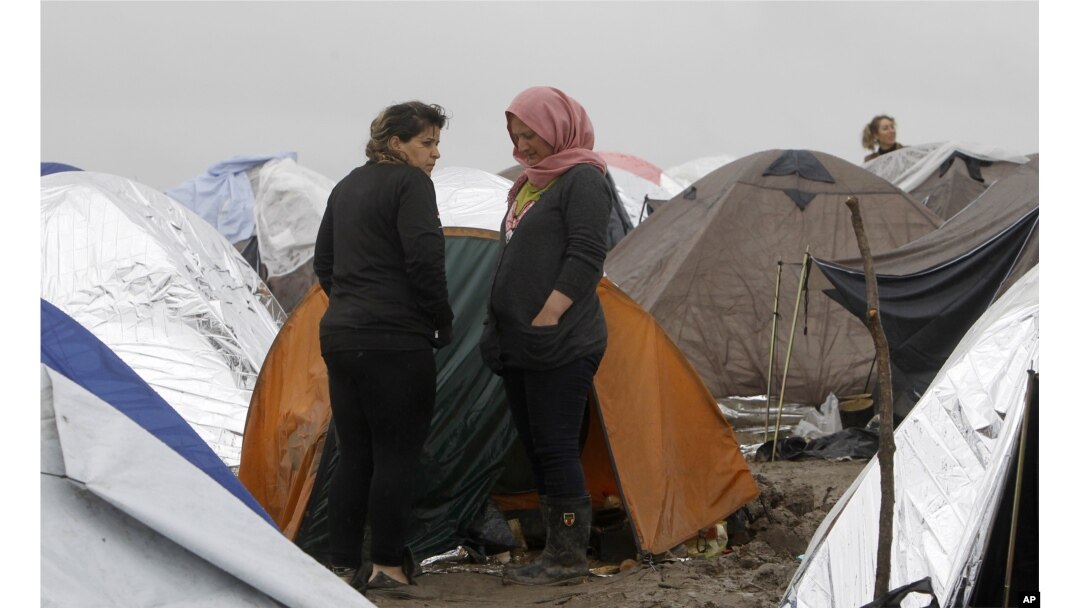 Syrian refugee women look on, standing in the mud between tents in an improvised camp on the border line between Macedonia and Serbia near the northern Macedonian village of Tabanovce, March 11, 2016.