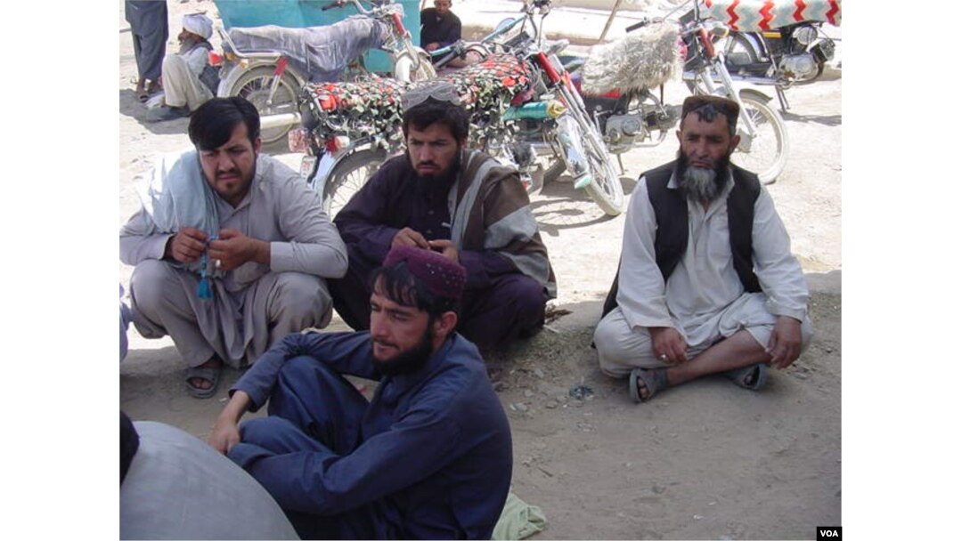Afghans waiting to return home sit in the shade of the customs office wall, Aug. 24, 2016. (Photo: A. Khan/VOA)