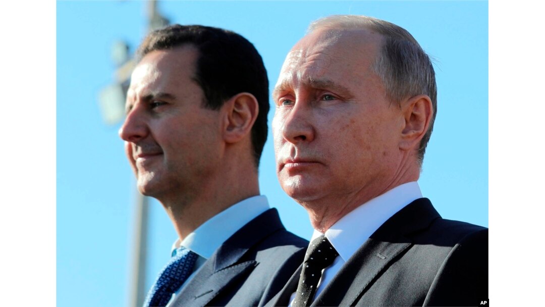 FILE - Russian President Vladimir Putin, right, and Syrian President Bashar al-Assad watch troops marching at the Hemeimeem air base in Syria, Dec. 11, 2017.