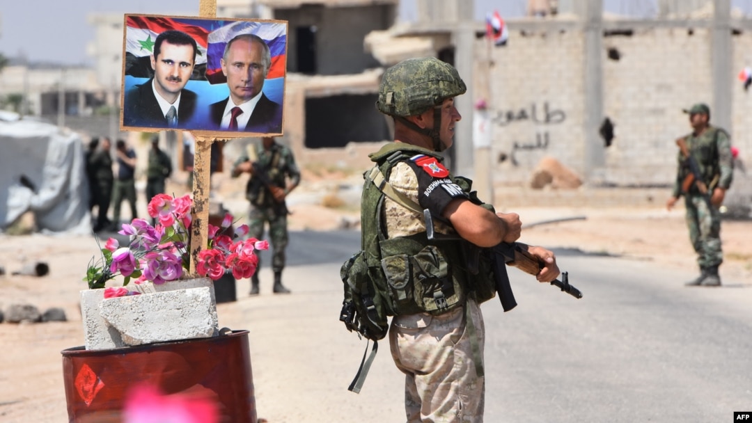 FILE - Members of Russian and Syrian forces stand guard near posters of Syrian President Bashar al-Assad and his Russian counterpart, Vladimir Putin, at the Abu Duhur crossing on the eastern edge of Idlib province, Syria, Aug. 20, 2018.