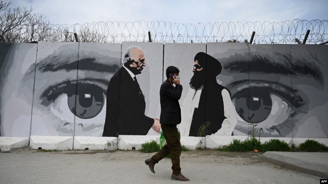 FILE - A man walks by a wall painted with images of U.S. Special Representative for Afghanistan Reconciliation Zalmay Khalilzad, left, and Taliban co-founder Mullah Abdul Ghani Baradar, in Kabul, April 5, 2020.
