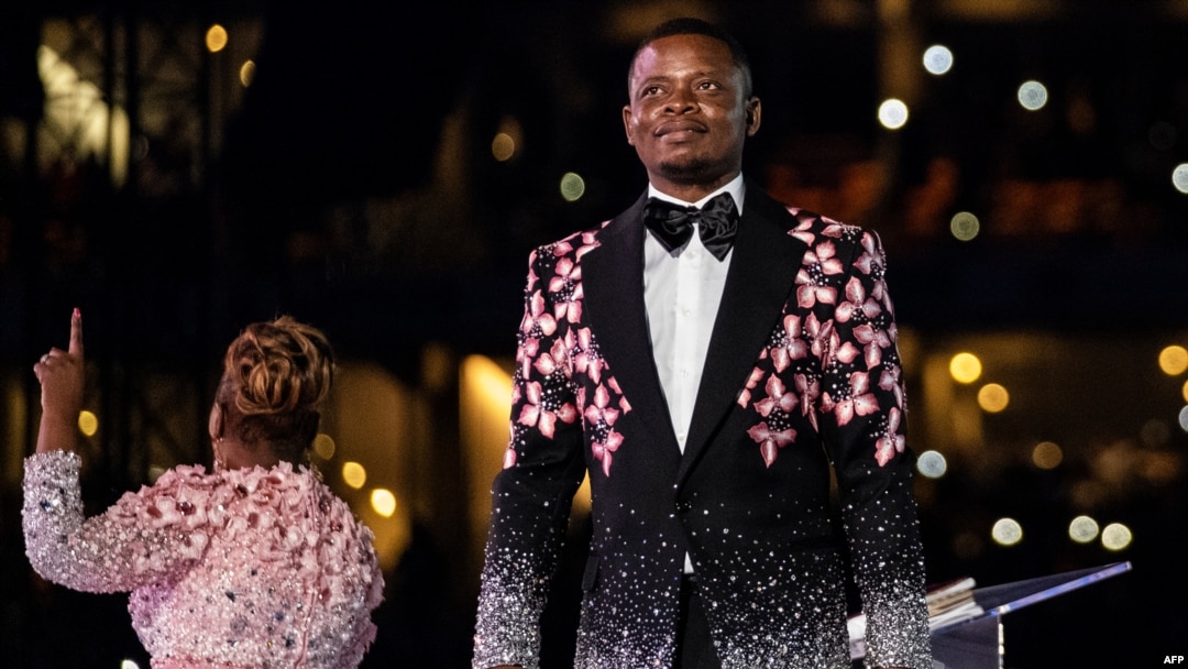 FILE - Pastor Shepherd Bushiri, right, from the Enlightened Christian Gathering stands on stage while his wife speaks to worshippers at the FNB Stadium in Soweto, Jan. 1, 2020.