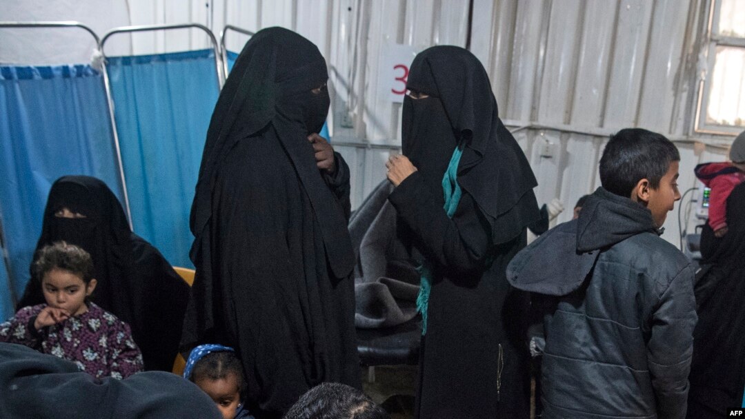 FILE - Two women, center, reportedly wives of Islamic State (IS) group fighters, wait with other women and children at a camp of al-Hol in al-Hasakeh governorate in northeastern Syria, Feb. 7, 2019.
