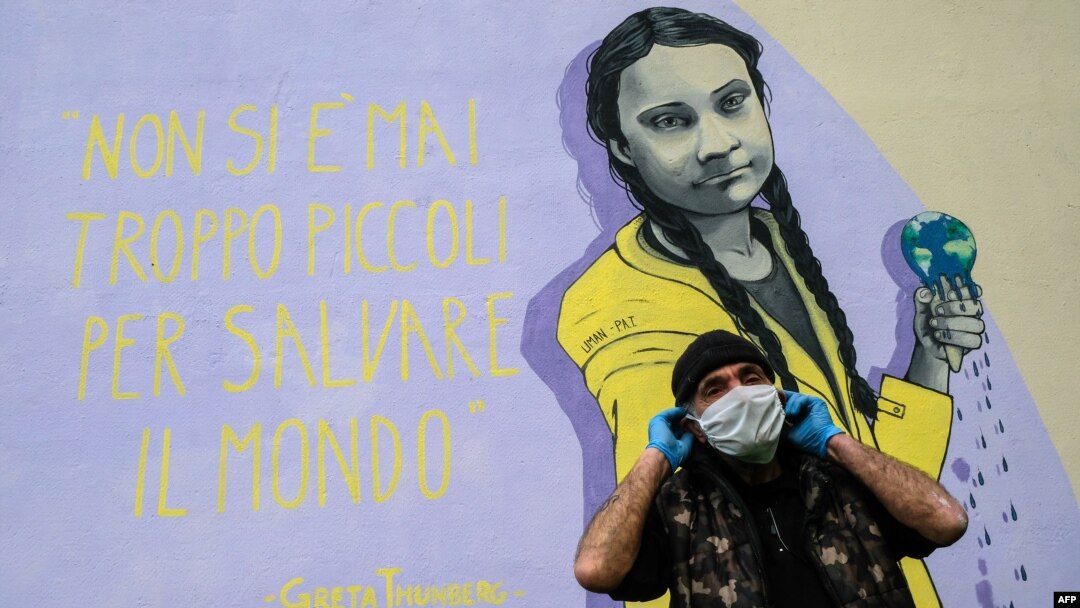 A resident wearing a face mask stands next to a mural featuring Swedish climate activist Greta Thunberg and her quote "You're never too young to save the world," in the Trullo district of Rome, March 30, 2020, during the COVID-19 pandemic.